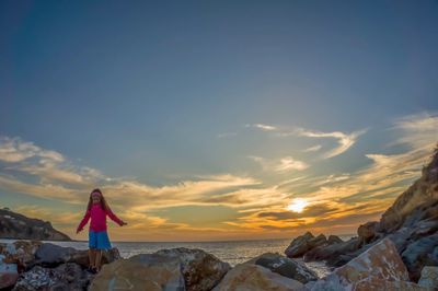 Woman standing on beach against sky during sunset