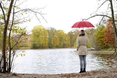 Rear view of woman holding umbrella standing by lake 