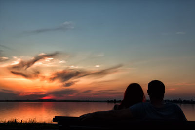 Silhouette couple sitting by sea against sky during sunset