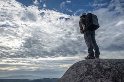 Rear view of backpack man standing on cliff against cloudy sky