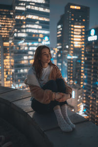 Young woman sitting on illuminated city at night