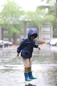 Full length of boy jumping over puddle on road during rainy season