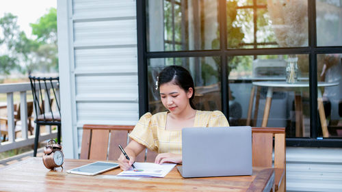 Young woman using phone while sitting on table