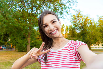 Portrait of smiling beautiful woman showing peace sign at park