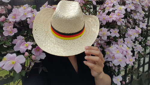 Close-up of woman holding straw hat against flowering plants