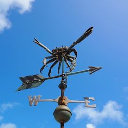 Low angle view of weather vane against blue sky