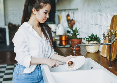 Young woman holding white while standing at home