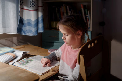 Boy looking at book while sitting on table at home