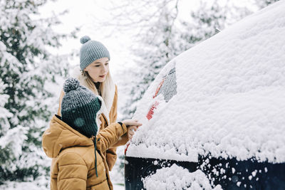 Boy helping mother to clear snow from car