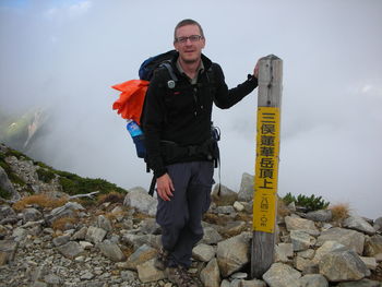 Portrait of man standing by information sign on mountain during fogy weather