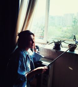 Side view of girl sitting on window at home