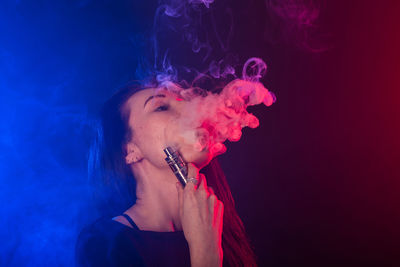 Portrait of man smoking cigarette against black background