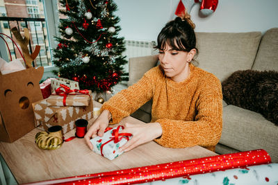 Full length of girl sitting on christmas tree at home