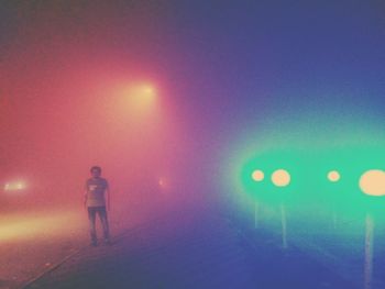 Rear view of man standing on illuminated street light at night