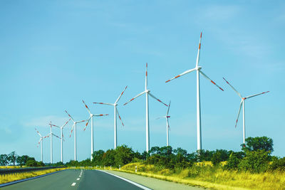 Road by wind turbines against sky