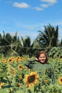 Portrait of smiling woman with sunflower against sky