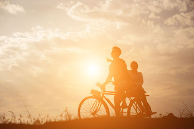 People riding bicycle against sky during sunset