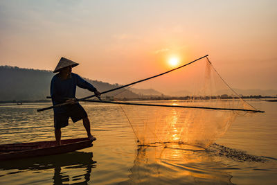 Man fishing in lake against sky during sunset