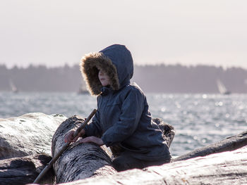 Man sitting on rock by sea against clear sky