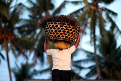 Rear view of man with basket walking against palm trees
