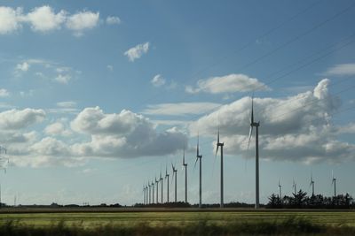 Electricity pylon on field against cloudy sky