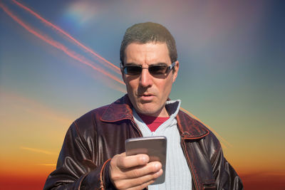 Mid adult man using mobile phone against sky