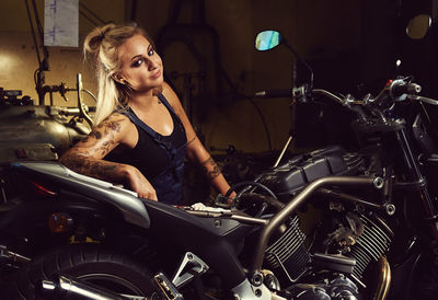 Portrait of young woman sitting by motorcycle at workshop
