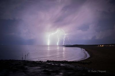 Panoramic view of lightning over sea against storm clouds