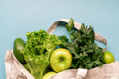 Food layout with apples, lettuce, cucumbers, limes, parsley in eco friendly bag on blue background