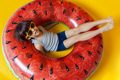 Boy in blue swimming trunks and sunglasses lying on an inflatable circle in the form of a watermelon