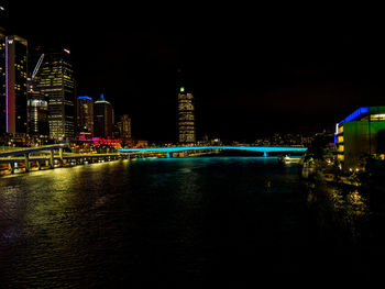 Illuminated buildings by river against sky at night