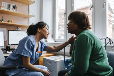 Female medical professional examining patient's neck while sitting in examination room