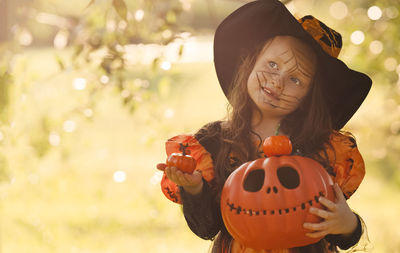 Pumpkin head jack-o'-lantern in the hands of a girl in a witch costume on outdoors with a copy space