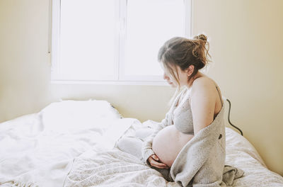 Young woman sitting on bed at home