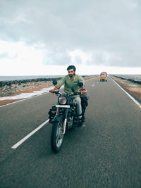 Man riding motorcycle on road by sea against sky