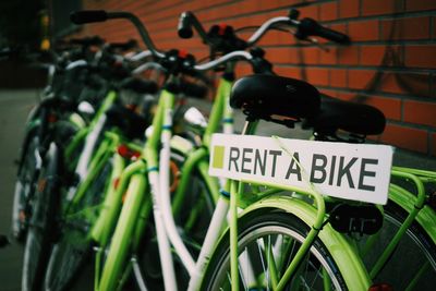 Green bicycles parked by brick wall for rent