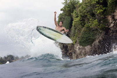 Young male surfer jumping over sea