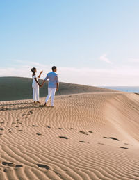 Rear view of people walking at beach against clear sky