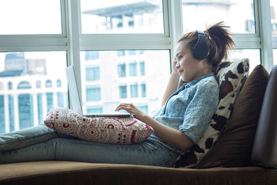 Side view of girl sitting on window at home