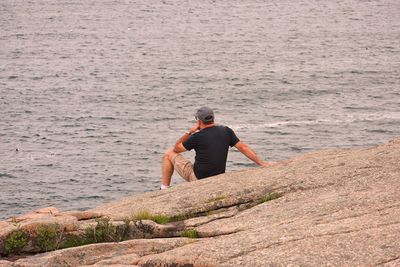 Rear view of man sitting on rock formation against sea