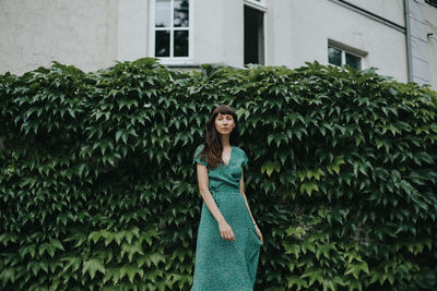 Portrait of beautiful woman standing against green leaves