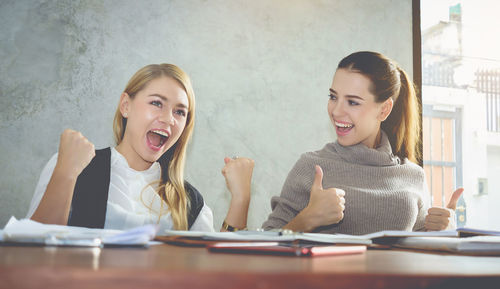 Happy businesswomen clenching fists and gesturing at office