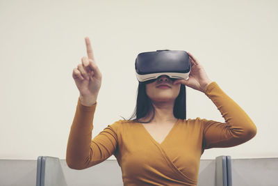 Woman wearing virtual reality simulator while pointing against clear sky