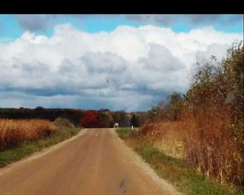 Road passing through field against cloudy sky