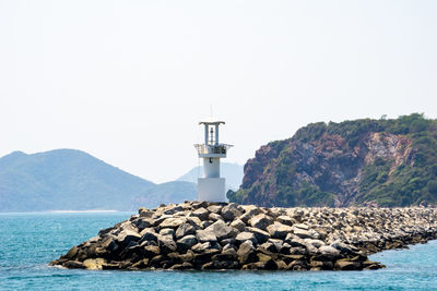 Lighthouse by sea against clear sky