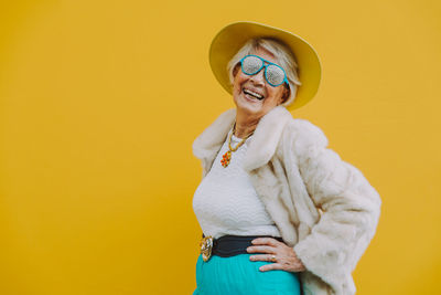 Portrait of smiling woman standing against yellow background