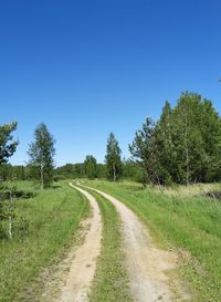 Empty road along trees on field against clear sky