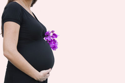 Midsection of pregnant woman standing over pink background