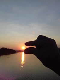 Close-up of silhouette hand against sea during sunset