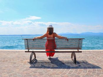 Rear view of woman sitting on bench at promenade against blue sky